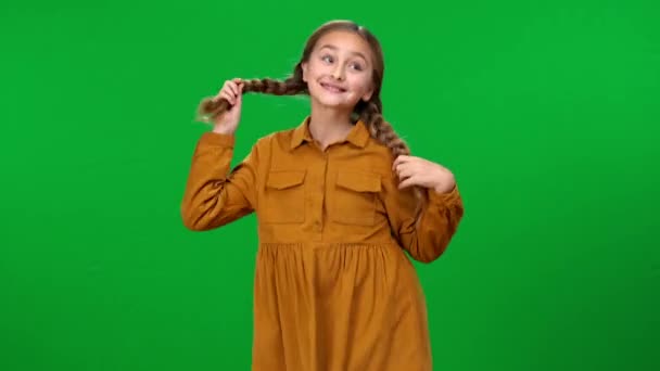 中镜头兴奋的女孩在绿色屏幕上跳舞 微笑着摸着辫子看着相机 快乐快乐的白人青少年在彩色键上快乐地摆姿势的正面形象 — 图库视频影像
