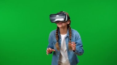Çevrimiçi sanal gerçeklik gözlükleriyle oyun oynayan heyecanlı beyaz kız yeşil ekran arka planına dönüyor. Mutlu genç oyuncu Chroma Key 'deki video oyununun tadını çıkarıyor.