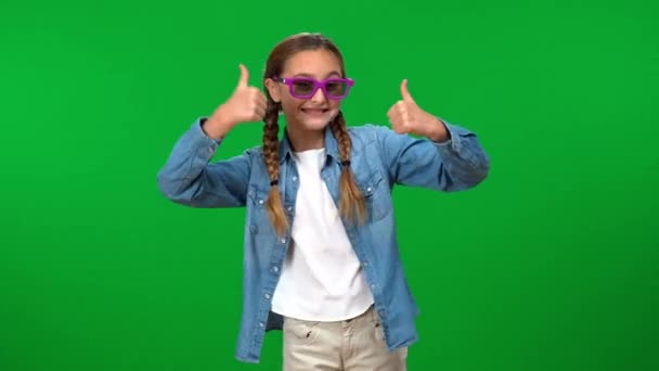 一个快乐的女孩在绿色的屏幕上摆着大拇指 戴着3D眼镜 青少年白种人青少年的画像 在色彩斑斓的背景上 带着淡淡的微笑看着相机 喜形于色 — 图库视频影像