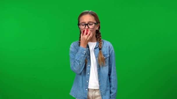中枪阳性白人女孩在眼镜咬咬苹果手放在髋部看着相机指向食指向上 智能青少年在绿色荧幕上摆姿势的肖像 — 图库视频影像