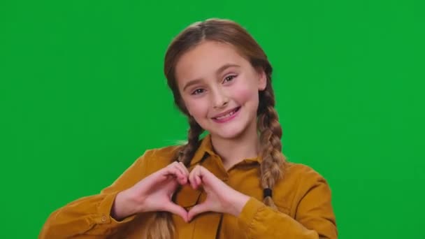 迷人的女孩的心形与手看着相机微笑在绿色的屏幕上 色键上漂亮的高加索少年近景肖像画 — 图库视频影像
