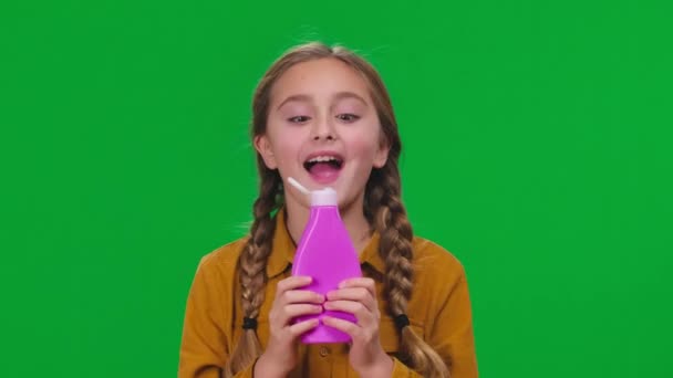 特写兴奋的女孩在绿色屏风下闻到粉色瓶子中洗发水淋浴露的芬芳 快乐而积极的白人青少年摆出一副色彩斑斓的背景微笑 — 图库视频影像
