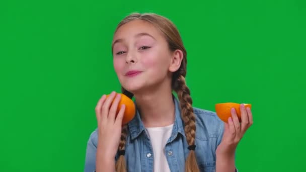 特写搞笑女孩舔橙色微笑看着相机在绿色屏幕上的鬼脸 浅色背景下素食水果的白人青少年轻松愉快的画像 — 图库视频影像