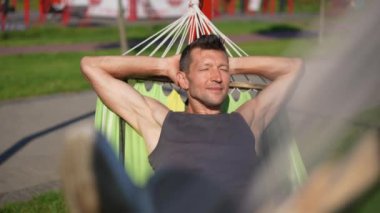 Ön manzara rahat yetişkin bir adam hamakta uzanmış, gözleri kapalı, keyfine bakıyor. Güneşli bahar gününde hafta sonu dinlenen tasasız, kaygısız beyaz adamın portresi.