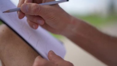 Güneşli bir bahar gününde erkek el açık havada resim çiziyor. Yakından tanınmayan beyaz adam tasarım yapıyor. Şehir parkında bankta oturuyor.