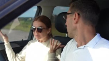 Kızgın Kafkasyalı koca, arabada yolcu koltuğunda oturan kızgın eşiyle tartışıyor. Güneşli bir günde arabada kavga eden sinirli bir çiftin portresi.