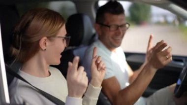 Bulanık bir adamla arabada dans eden neşeli kadın gülümseyerek el kol hareketi yapıyor. Neşeli Kafkasyalı evli çift güneşli bir günde otomobilde eğleniyor.