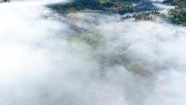 カルパチア山脈の穏やかな村の上に白い霧の中にドローンダイビング 広いショット空中ビュー朝の高地の霧の中で小さな町 — ストック動画