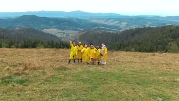 黄色の雨のコートの興奮した人々のグループは ドローンのズームアウトとしてカメラを見て手を振った 幸せな正白人男性と女性のポーズカルパチア山脈の風景 — ストック動画