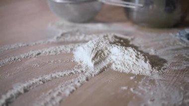 Yakından tanınmayan kadın aşçı masaya beyaz unu yavaş çekimde yayıyor. Ahşap masa üstünü pişirme malzemesiyle kaplayan eldivenli kadın eli.