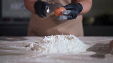 Yavaş çekimde beyaz un yığınında çırpılmış yumurta. Önlüklü ve eldivenli tanımlanamayan beyaz kadın mutfakta lezzetli yemekler pişiriyor.