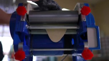 Hamur makinesini kapat, hamuru yuvarla ve kadın eli eldivenle dışarı çıkar. Tanımlanamayan Kafkasyalı aşçı yakın plan hamur işi pişiriyor.