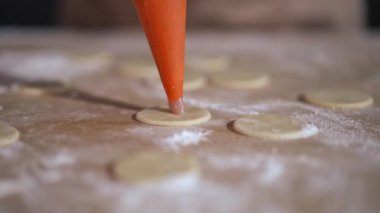 Yuvarlak hamur çemberinde pişen şırıngadan öğütülen et. Yakından tanınmayan kadın aşçı mutfakta hamur tatlısı hazırlıyor.