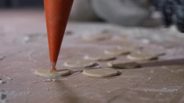 Yakın plan eldivenler, yuvarlak hamur çemberlerinde pişen şırıngadan öğütülen et. Yakından tanınmayan beyaz kadın aşçı mutfakta hamur köftesi hazırlıyor.