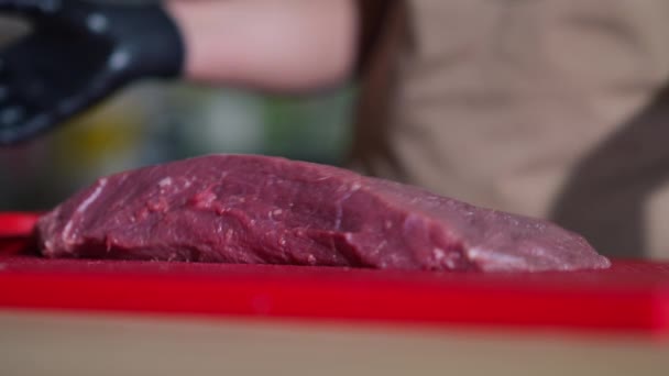用女手用锋利的刀切肉 将新鲜的小牛肉放在切菜板上 身着手套 面目全非的白人厨师在餐馆准备生料做饭 — 图库视频影像