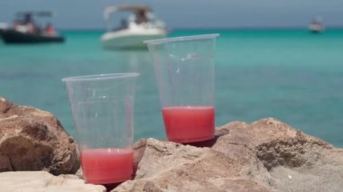 Yakın plan plastik bardaklar, arka planda kırmızı meyve suyu ve yatlı Akdeniz 'in mavi gölü. Turist beldesinde gün ışığında serinletici bir içecek.