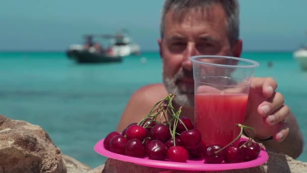 果実とぼやけた男が背景にさわやかなジュースを飲んでクローズアッププレート 幸せな白人男性観光客キプロスの地中海のラグーンで休暇を楽しむ — ストック動画