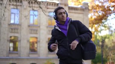 Neşeli, kendine güvenen, kulaklıklı Afro-Amerikan genç adam dans edip dışarı çıkıyor. Üniversite kampüsünde hobisiyle gezen mutlu öğrenci.