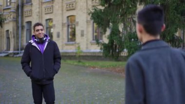 Pozitif Afro-Amerikalı genç adam, yavaş çekimde ayrılan Kafkas grup arkadaşını selamlıyor. Üniversite kampüsünde gezen zeki, kendine güvenen mutlu öğrenciler.