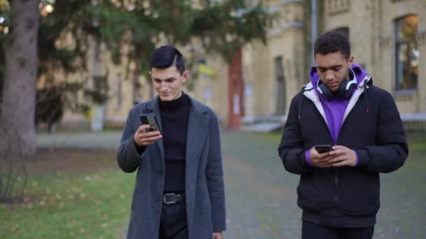 Два Абсорбированных Студента Прогуливаются Улице Прокручивая Приложение Смартфоне Делая Селфи — стоковое видео