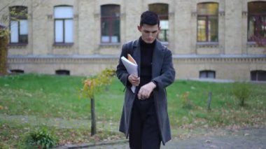 Erkek üniversite öğrencisi çıkış saatini kontrol ediyor. Kampüste aceleyle genç bir beyaz adamın portresi.