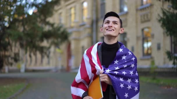 スローモーションで見て回るアメリカ国旗の幸せな満足した男 自信満々の大学生の肖像 屋外のキャンパス — ストック動画