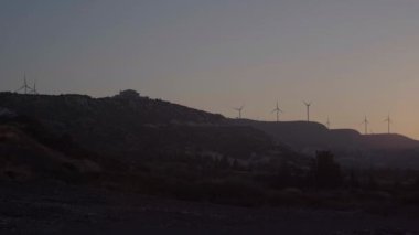 Canlı kamera soldan sağa dönüyor alacakaranlıkta dağlarda dönen rüzgar türbinleri gibi. Yel değirmenleriyle Kıbrıs 'ın geniş açılı gün batımı manzarası