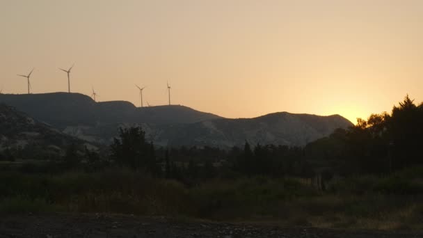 空を背景にスローモーションで回転する夕日の光と風車の広いショット牧草地や山 キプロスの夏の風景屋外夜 — ストック動画