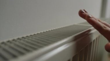 Yakın çekimde beyaz kadın radyatöre dokunarak evde ısıyı kontrol ediyor. Tanımlanamayan kadın ve ısıtma cihazı içeride.