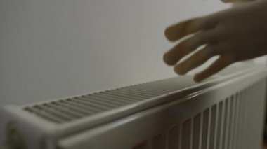 Kapalı kalorifer kaloriferi ve sağ tarafta avuçlarını ısıtan beyaz eldivenli kadın elleri. Soğuk dairede tanınmayan bir kadın.