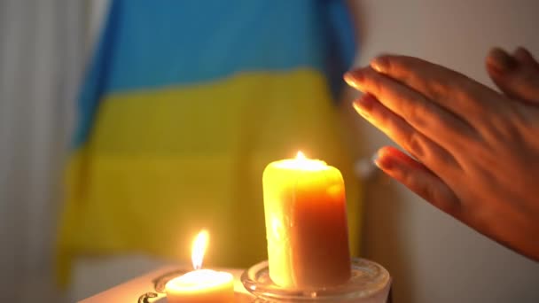 閉じる側のビュー認識できない女性ウクライナのフラグの背景にある燃焼キャンドルで右側に手をこすり キエフで停電中の若い白人女性の温暖化ヤシウクライナ — ストック動画