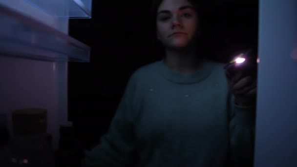 懐中電灯を閉じドアでジャムの暗闇の中で冷凍庫を開く若い女性の冷蔵庫の中からの眺め 停電中に家で食べ物を探している美しい白人女性 — ストック動画