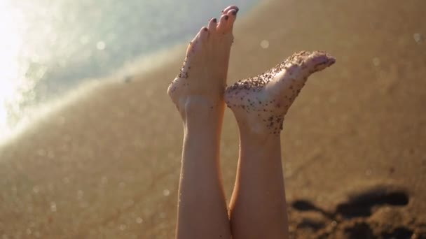 地中海の黄金の砂と青い水を背景に若い女性の閉鎖足 目に見えない白人日焼けしたリラックスした女性のクローズアップ足太陽の下でビーチに横たわっている — ストック動画