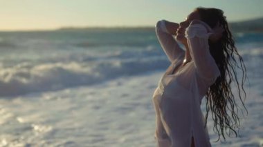 Akdeniz 'in arka planında kıyıya yavaş çekimde vuran muhteşem ince kadın. Gün batımında plajda kendine güveni tam beyaz bir turist.