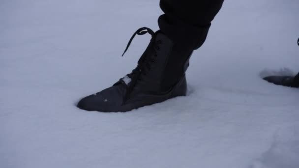 遅い動きで白い冬の雪の中で男性の足のショットの手順を追跡します 黒革のブーツで認識できない男で屋外でのクローズアップ — ストック動画