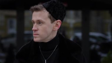 Yakın plan LGBT çalışanı şehir caddesinde yavaş çekimde kahve içiyor. Mutlu, kendine güvenen, beyaz eşcinsel adam açık havada lezzetli bir içkinin tadını çıkarıyor.