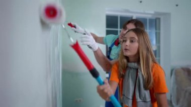 Duvarı boyayan çok tatlı bir genç kız arka planda genç adamın konuşmasına yardım ediyor. Babasıyla oturma odasının yenilenmesi için kendine güvenen beyaz bir kızın yan açılı portresi.