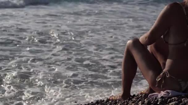 无法辨认的瘦弱的晒黑的女人坐在右边的卵石沙滩上 就像在阳光下翻滚在海岸上的地中海波浪 白种人自信放松的观光客享受日落 — 图库视频影像