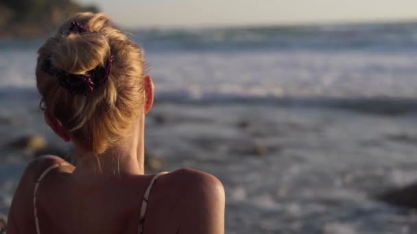 地中海のビーチに座っているリラックスした女性の肩の上に黄金の夕日を眺めながら撮影します キプロスで夕暮れ時に日光浴を楽しむ白人観光客に満足 — ストック動画