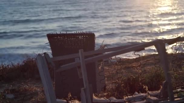 地中海のビーチで日没時に壊れたアームチェアとテーブル 海の海岸に人がいない夕暮れ時に閉鎖放棄された家具 環境汚染の概念 — ストック動画