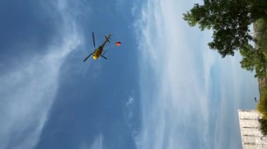 Madrid, İspanya - 16 Mayıs 2023: İnsanlar uçakları izlerken su deposuna geçen sarı ateş helikopterinin dikey videosu. Geniş çekim kurtarma ekibi itfaiye konusunda çalışıyor.