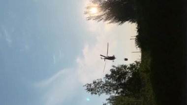 İspanya 'da gün batımında su deposundan yükselen yangın helikopterinin dikey video silueti. Kurtarma uçakları dışarıdaki geniş ateşi söndürüyor.