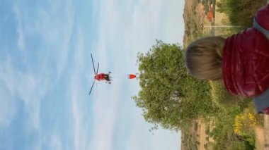 Gökyüzünde uçan kırmızı ateş helikopterine bakan, tanınmayan sarışın bir kadının kafasının arkası. Beyaz kadının açık havada kurtarma uçaklarını izlediği dikey bir video.