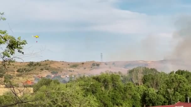 屋外で晴れた夏の日に火の上に水を放出煙の上を飛んでワイドショット黄色の消防ヘリコプター スペインの山の丘で大きな火災を消火する消防士 — ストック動画