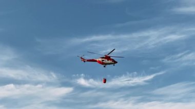 Madrid, İspanya - 16 Mayıs 2023: Mavi bahar gökyüzünde suyla uçan kırmızı ateş helikopteri. Kurtarma helikopterinin dışarıdaki yangını söndürme görüntüsü.