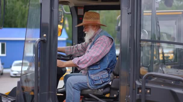 坐在拖拉机上的快乐的老年农民的宽镜头侧视 转身看着相机 竖起大拇指 心满意足的白人男子在室外收割机中慢动作地摆姿势 — 图库视频影像