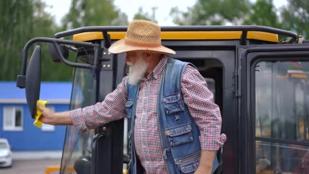 老年男性农民清洁后视镜进入驾驶舱时坐在驾驶座上 在户外大型农业机械中自信而有经验的白胡子男人 — 图库视频影像
