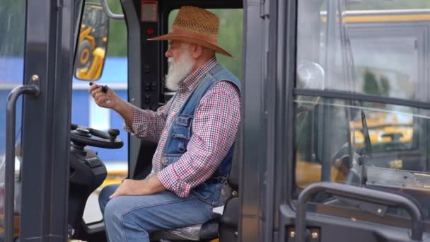 キャビンに座ってスローモーションで農業用収穫機のエンジンを開始シニア白人男性 トラクターの屋外でオンに自信のある専門家農家のサイドビューの肖像画 — ストック動画