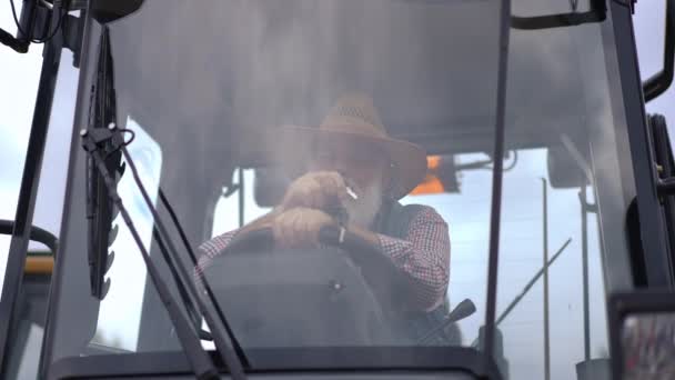 射击通过挡风玻璃的资深白人男子坐在巨大的拖拉机机舱打开引擎与钥匙 户外运动中自信的职业农艺师 — 图库视频影像