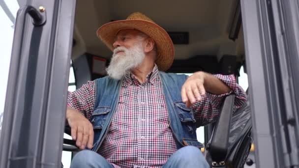 老农民坐在拖拉机上慢吞吞地四处张望 心满意足的白种人老人在户外享受收获季节的正面肖像 — 图库视频影像
